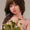 TAYU Doll Chiori 160cm doll with brown braided hair, soft makeup, pink dress, stockings, and seated floral styling.